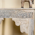 Close up side image of a handcrafted reclaimed teak wood console table with sandblasted finish, carved floral detailing, vintage corbels, and lower shelf; perfect for styling with vintage home accessories, 133 × 62 × 90 cm.