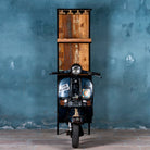 Front image of a high bar table featuring the front half of a vintage Bajaj scooter, with tall wooden shelving and an industrial metal frame, designed for stylish bar storage.