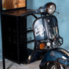 Close p image of a high bar table featuring the front half of a vintage Bajaj scooter, with tall wooden shelving and an industrial metal frame, designed for stylish bar storage.