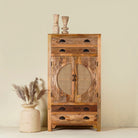 Hand carved mango wood cupboard with rattan inserts, featuring four drawers and two inner compartments, placed against a neutral background with a small vase and rattan decoration.