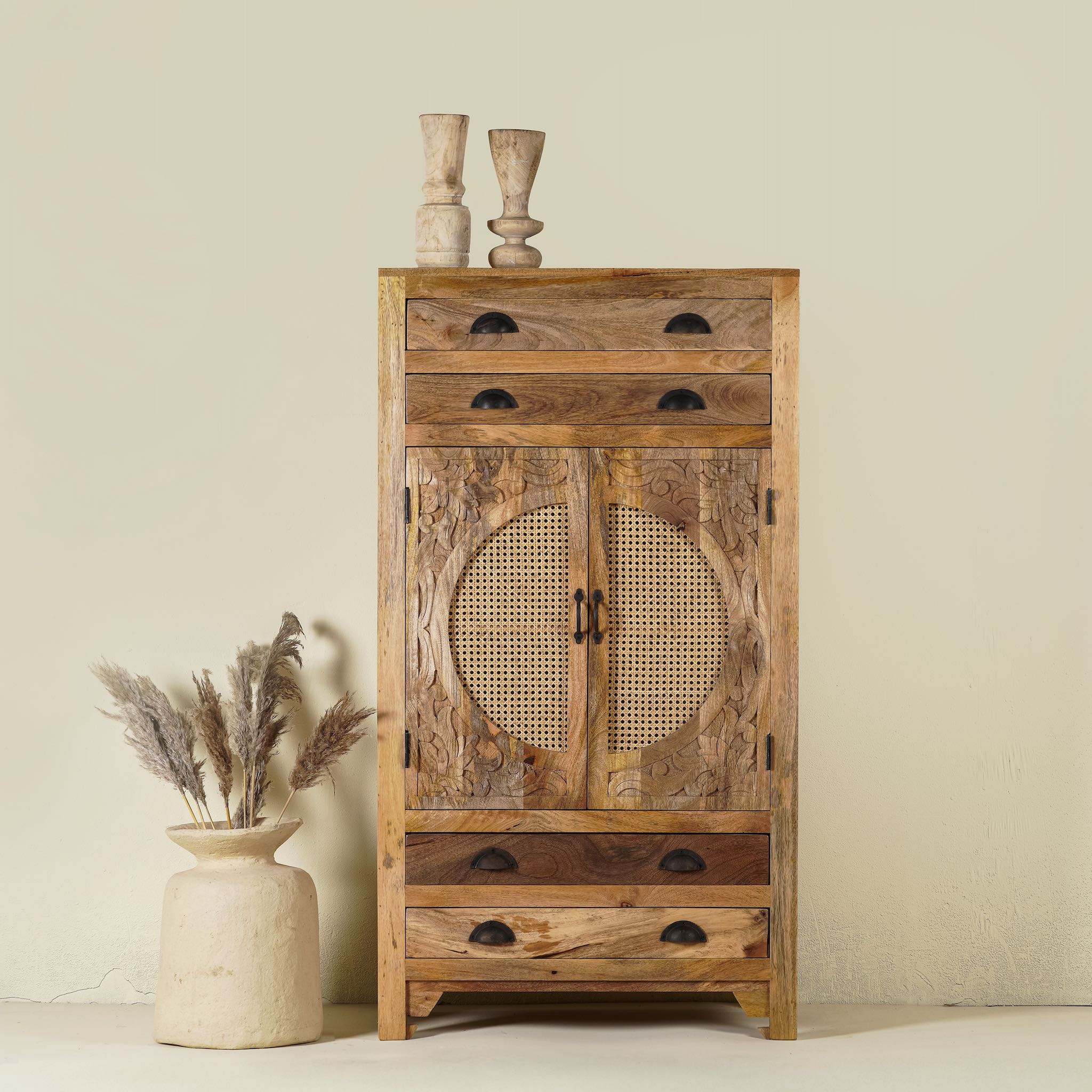 Hand carved mango wood cupboard with rattan inserts, featuring four drawers and two inner compartments, placed against a neutral background with a small vase and rattan decoration.