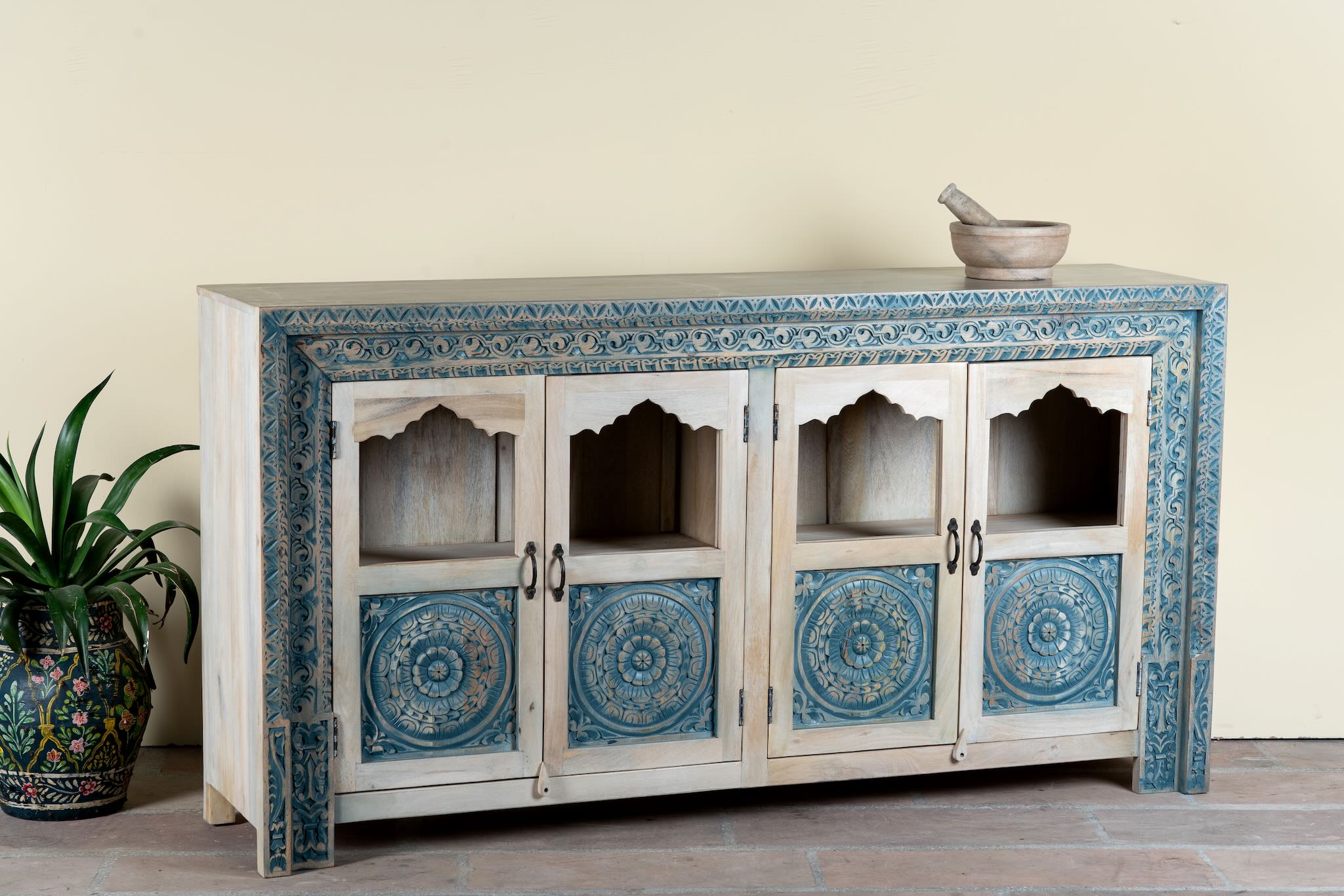 Side angle image of a hand carved showcase made of natural mango wood in white washed with blue floral accents and half glass doors in vintage design.