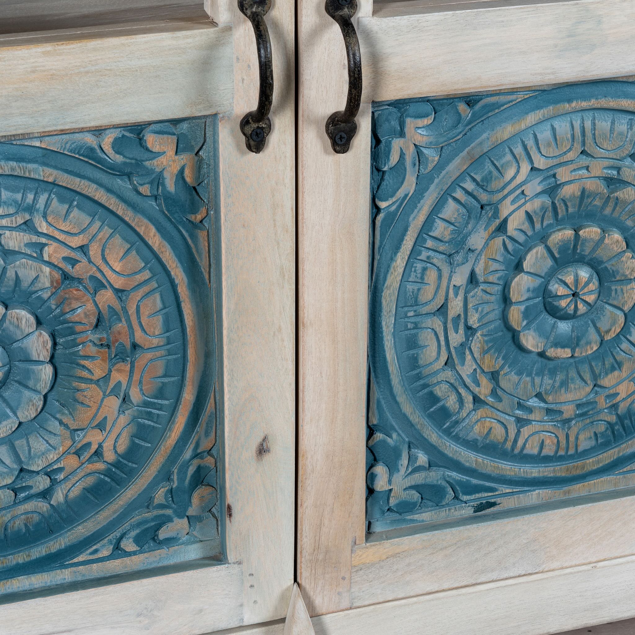 Close up image of a hand carved showcase made of natural mango wood in white washed with blue floral accents and half glass doors in vintage design.