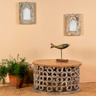 A hand-carved mango wood coffee table with a natural wood top and a vintage multicolored base, displayed in a room with decorative items.