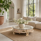 Life style image of a round reclaimed teak coffee table with glass top and hand-carved base; rustic vintage design, 84 cm diameter, 28 cm height.