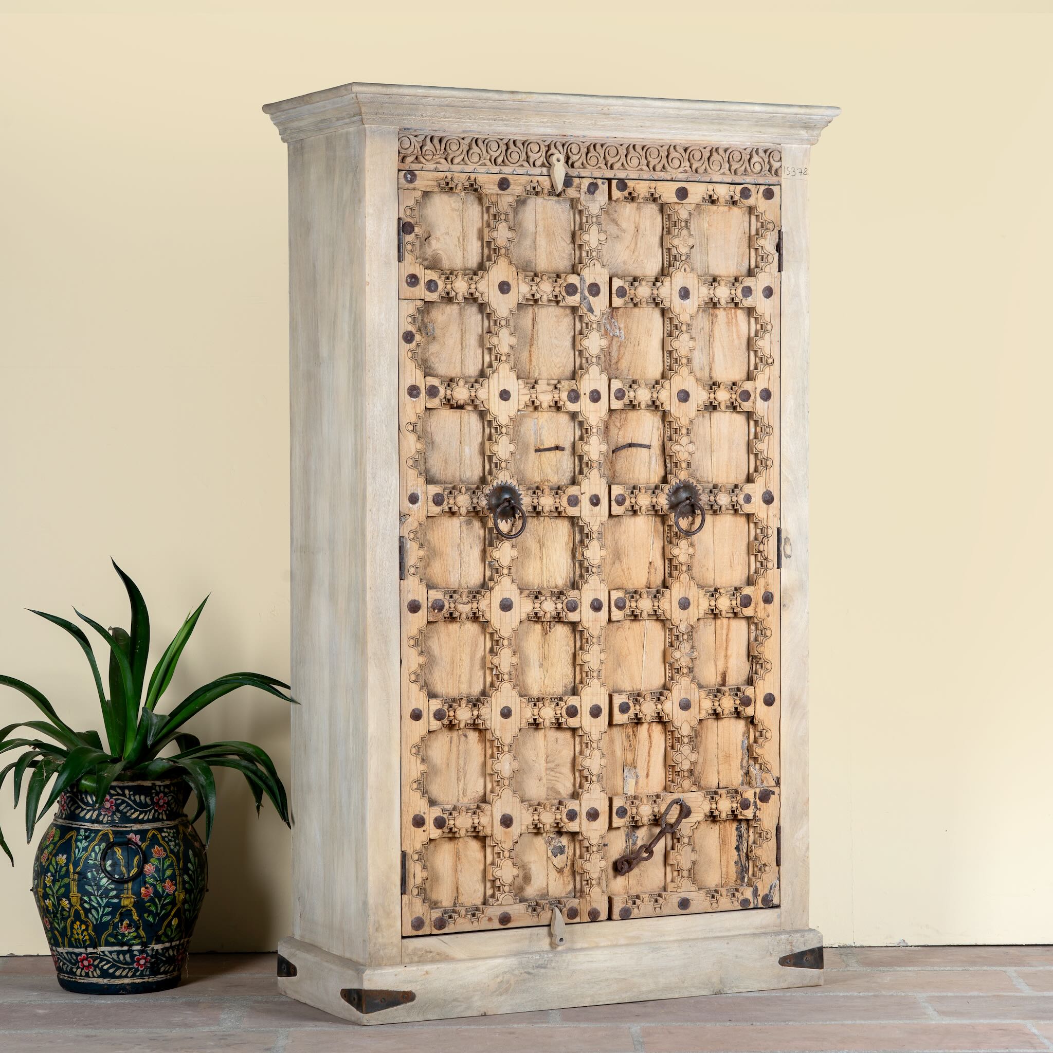 Side angle image of a reclaimed wood wardrobe Akhila featuring an old Indian door front with carved details and iron hardware. A sustainable furniture piece and unique old door cabinet for soulful, heritage-inspired interiors.