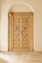 Wooden door with decorative carvings in a beige archway.
