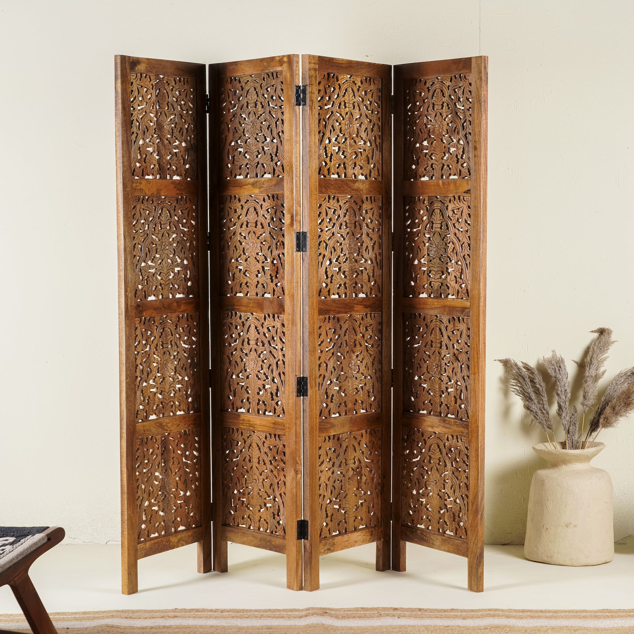 Foldable room partition made from mango wood, featuring four panels with intricate hand-carved floral and lattice designs, finished in a warm natural tone and connected by black metal hinges for flexible positioning.
