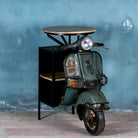 Side angle image of a short bar table crafted from the front half of an original Bajaj scooter, featuring a round wooden top, metal frame, and rustic industrial finish.