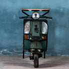Front image of a short bar table crafted from the front half of an original Bajaj scooter, featuring a round wooden top, metal frame, and rustic industrial finish.