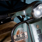 Close up image of a short bar table crafted from the front half of an original Bajaj scooter, featuring a round wooden top, metal frame, and rustic industrial finish.