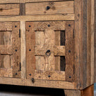 Close up image of a rustic design sideboard made from reclaimed wood with panelled doors, drawers, and iron accents; 150 × 40 × 90 cm.