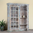 Side angle image with open door of a reclaimed wood display cabinet Amara with distressed turquoise finish and glass-panelled doors. Sustainable living room furniture and vintage furniture piece with spacious shelving and authentic patina.
