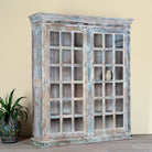 Side angle image of a reclaimed wood display cabinet Amara with distressed turquoise finish and glass-panelled doors. Sustainable living room furniture and vintage furniture piece with spacious shelving and authentic patina.
