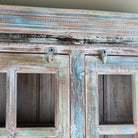 Close up image of a reclaimed wood display cabinet Amara with distressed turquoise finish and glass-panelled doors. Sustainable living room furniture and vintage furniture piece with spacious shelving and authentic patina.