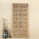 Hand-carved sliding door panel made from reclaimed wood, featuring symmetrical floral motifs in square reliefs for a warm, artisanal statement piece.