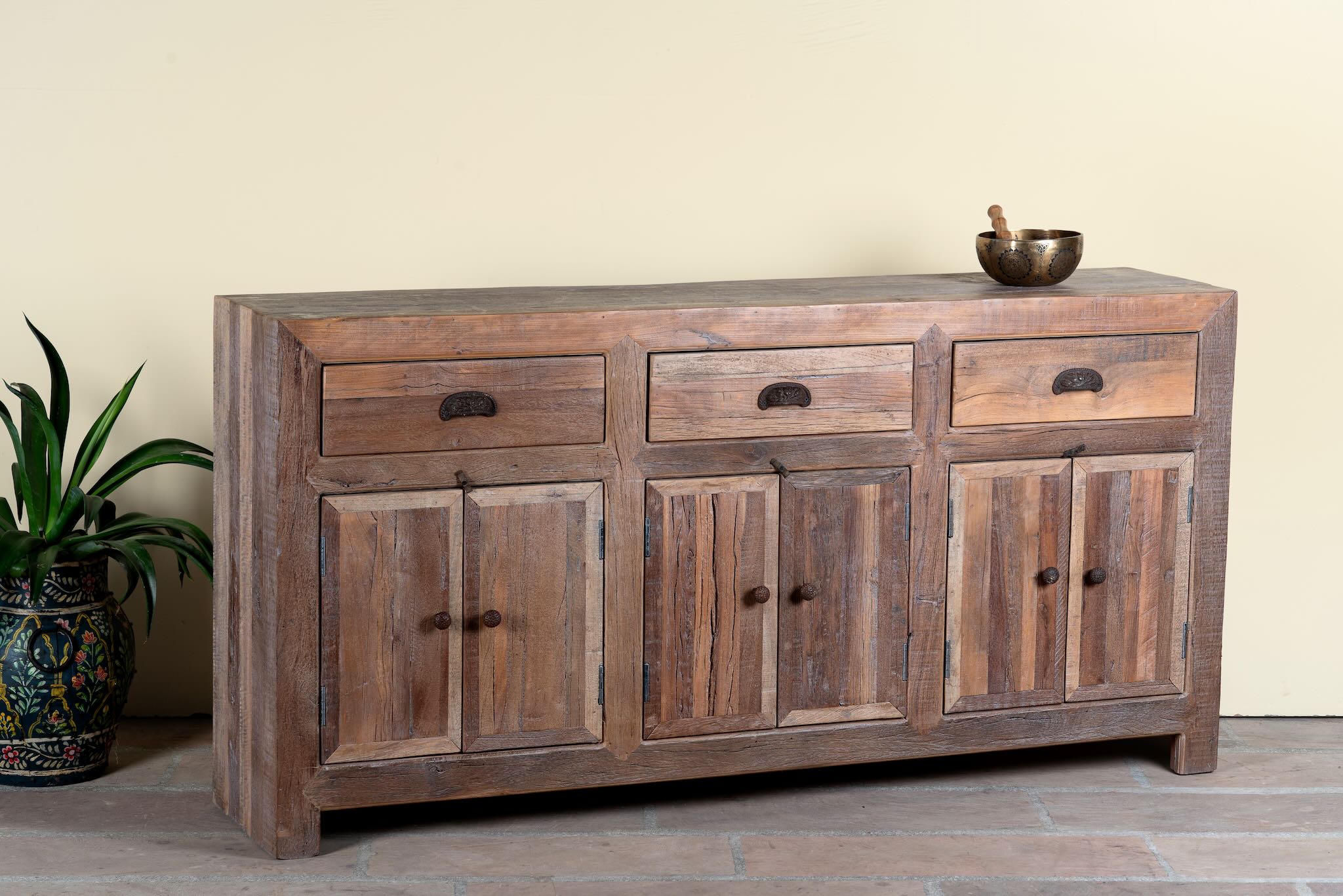 Side angle image of a reclaimed wood sideboard Amira in a rustic minimalist design, featuring three drawers and six doors with iron handles. A sustainable piece of living room furniture with natural textures and timeless appeal.