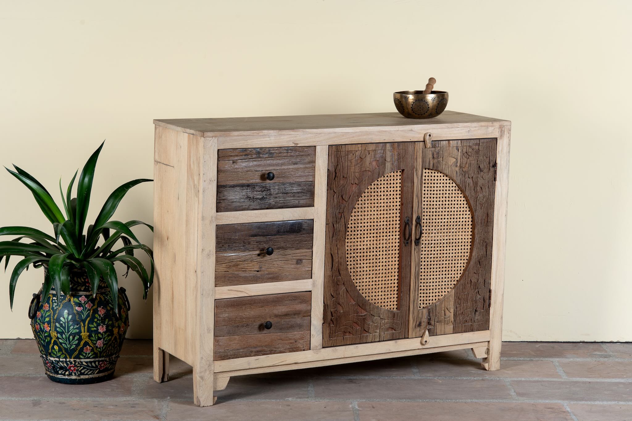 Side angle image of a reclaimed wood sideboard Amruta with three drawers and rattan-inlay cabinet doors in a circular design. A piece of sustainable furniture blending rustic wood textures and handcrafted detail.
