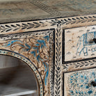 Close up image of a hand-painted sideboard Anaya made from reclaimed wood with six drawers and two glass doors, featuring detailed animal and floral motifs. A sustainable piece of boho-style artisanal furniture with colourful heritage design.