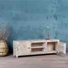 Open door image of a white washed mango wood lowboard with carved floral doors and open shelving, 180 × 40 × 60 cm.