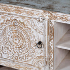 Close up picture of a white washed mango wood lowboard with carved floral doors and open shelving, 180 × 40 × 60 cm.