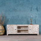 White washed mango wood lowboard with carved floral doors and open shelving, 180 × 40 × 60 cm.