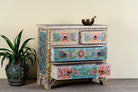 Side angle image with open drawers of a Hand-painted chest of drawers Anjana made from reclaimed wood, featuring four drawers with floral motifs in vibrant colours. A standout piece of sustainable furniture and painted wooden artistry.