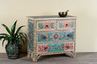 Side angle image of a hand-painted chest of drawers Anjana made from reclaimed wood, featuring four drawers with floral motifs in vibrant colours. A standout piece of sustainable furniture and painted wooden artistry.