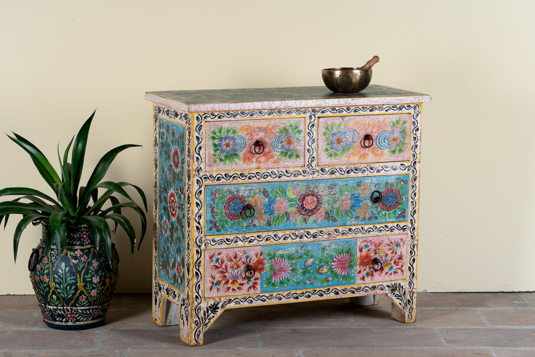 Side angle image of a hand-painted chest of drawers Anjana made from reclaimed wood, featuring four drawers with floral motifs in vibrant colours. A standout piece of sustainable furniture and painted wooden artistry.