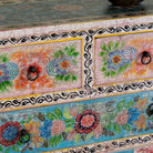 Close up image of a hand-painted chest of drawers Anjana made from reclaimed wood, featuring four drawers with floral motifs in vibrant colours. A standout piece of sustainable furniture and painted wooden artistry.
