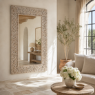 Lifestyle image of a carved wood mirror Antaka made from solid mango wood with hand-carved frame. A unique piece of living room furniture and boho wall décor that adds light and rustic elegance to any space.