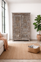 Lifestyle imagination of a reclaimed teak wood cabinet Atharva with floral hand-carved doors in a vintage distressed finish. A sustainable furniture piece ideal for rustic and character-rich living room interiors.