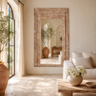 Lifestyle image of a carved wood mirror Anushara made from hand-carved mango wood with floral motifs and distressed finish. A bold piece of living room furniture ideal for boho and coastal-inspired spaces.