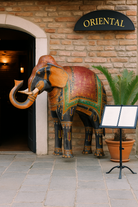 Lifestyle scene with a large hand-painted decorative elephant sculpture made of sheet metal in vibrant Rajasthani style, featuring intricate floral and geometric patterns in red, green, and gold. Ideal for enhancing entrance areas, restaurant lobbies, hotel receptions, or luxury interior spaces.