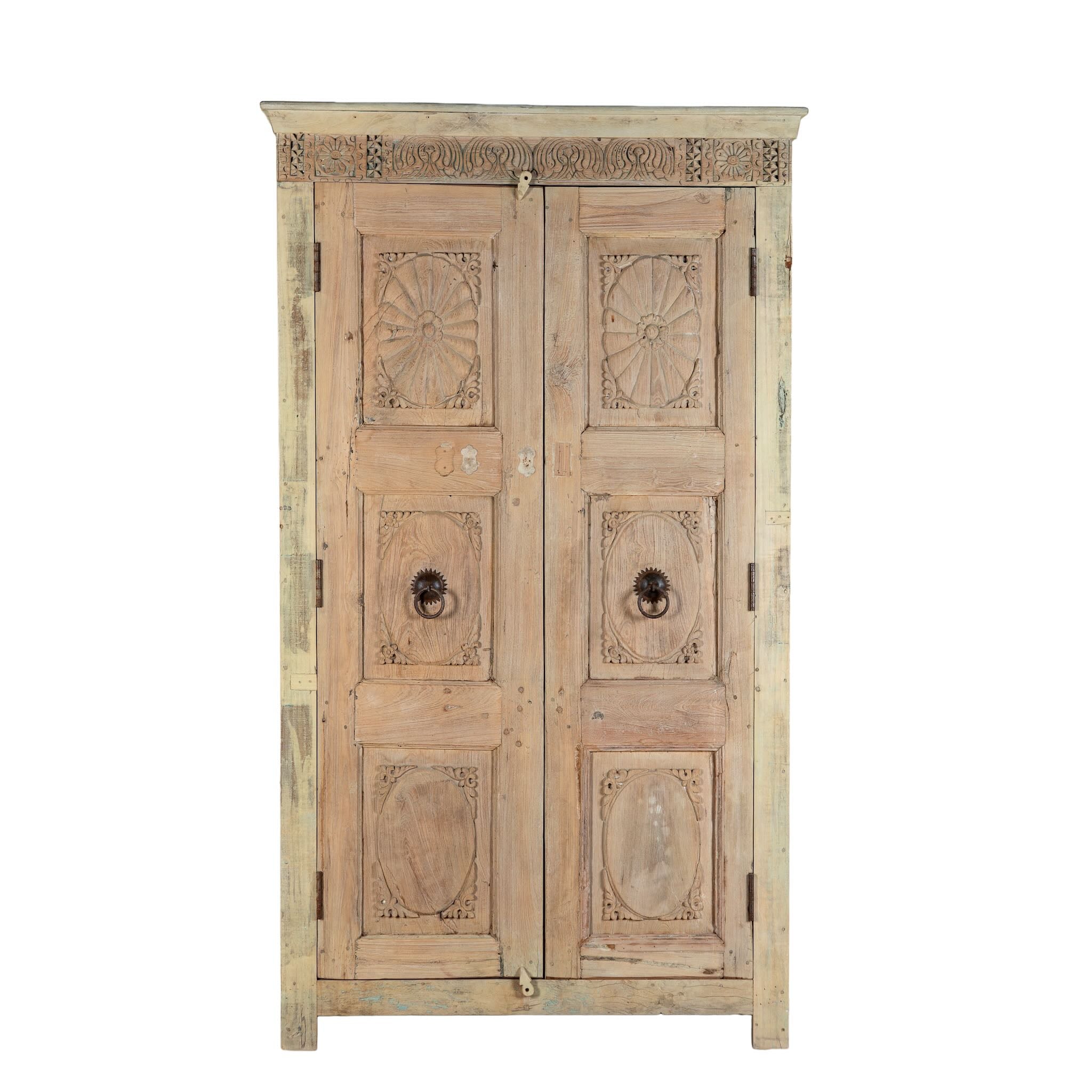 White background image of a reclaimed teak wood cabinet Anwika featuring a tall Mediterranean-style frame with hand-carved antique Indian doors. A unique piece of Indian furniture offering character-rich storage and timeless design.