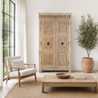Lifestyle imagination of a reclaimed teak wood cabinet Anwika featuring a tall Mediterranean-style frame with hand-carved antique Indian doors. A unique piece of Indian furniture offering character-rich storage and timeless design.