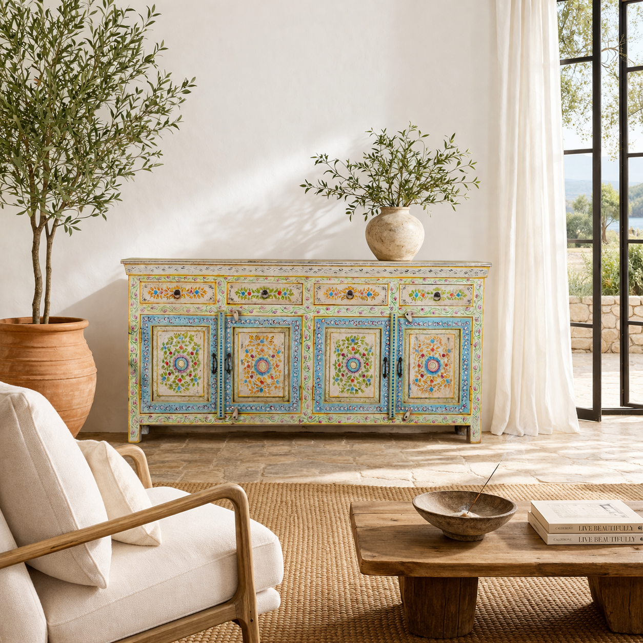 Lifestyle imagination of a hand-painted reclaimed wood cabinet Anwita in Mediterranean Boho style with floral motifs, four drawers, and four doors. A colourful and sustainable statement piece for boho chic living room décor.