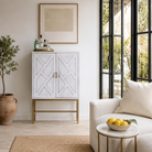 Lifestyle image of a tall whitewashed mango wood cabinet with carved lines and antique brass iron base, 91 × 154 × 43 cm.