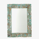 White background image of a carved mango wood mirror Apasmara in distressed turquoise finish with floral motifs. A handcrafted piece of Indian furniture ideal for vintage home decor and colourful boho interiors.