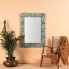 Carved mango wood mirror Apasmara blue in distressed turquoise finish with floral motifs. A handcrafted piece of Indian furniture ideal for vintage home decor and colorful boho interiors.