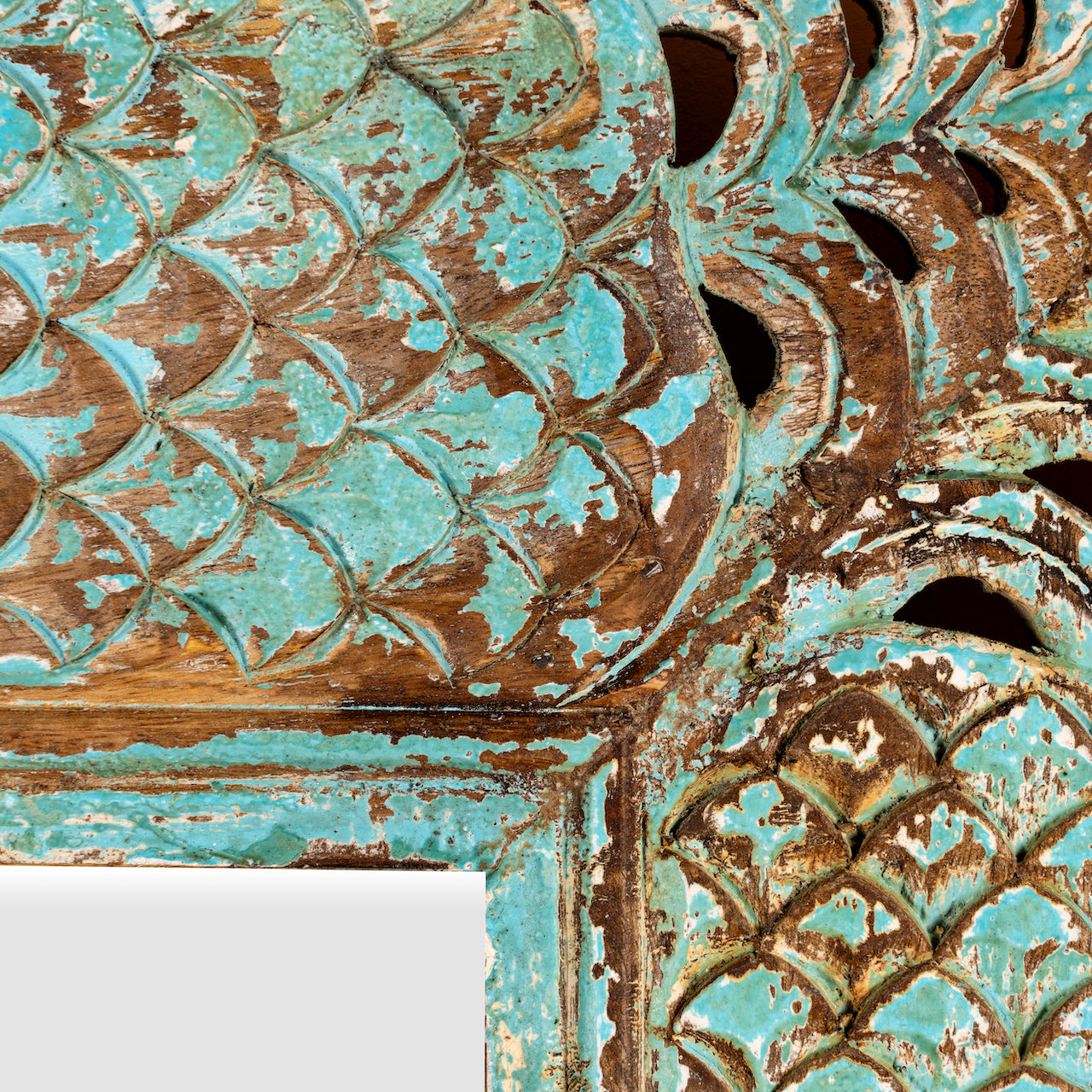 Close up image of a carved mango wood mirror Apasmara blue in distressed turquoise finish with floral motifs. A handcrafted piece of Indian furniture ideal for vintage home decor and colourful boho interiors.