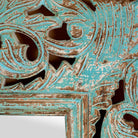 Close up image of a carved mango wood mirror Apsara blue in distressed turquoise finish with intricate hand‑carved floral details. A unique piece of Indian furniture online ideal for vintage home decor and boho interiors.
