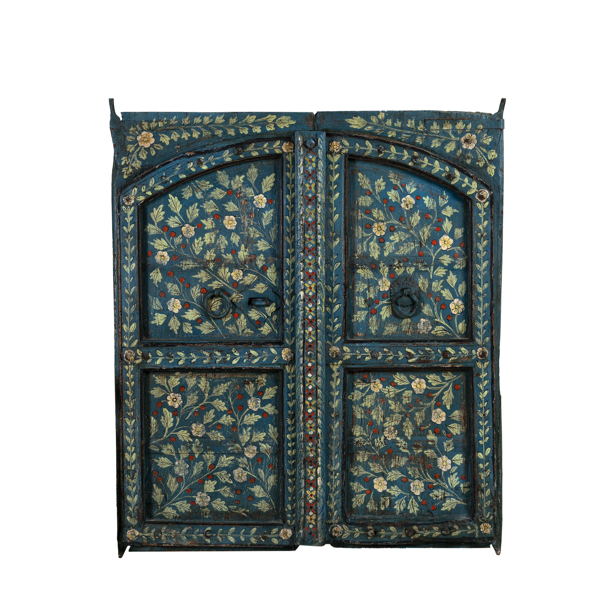White background image of a vintage wall panel crafted from an old teak wood window frame, hand-painted with detailed floral designs in cream, red, and green on a rich teal background, featuring arched upper panels and decorative metal ring pulls.
