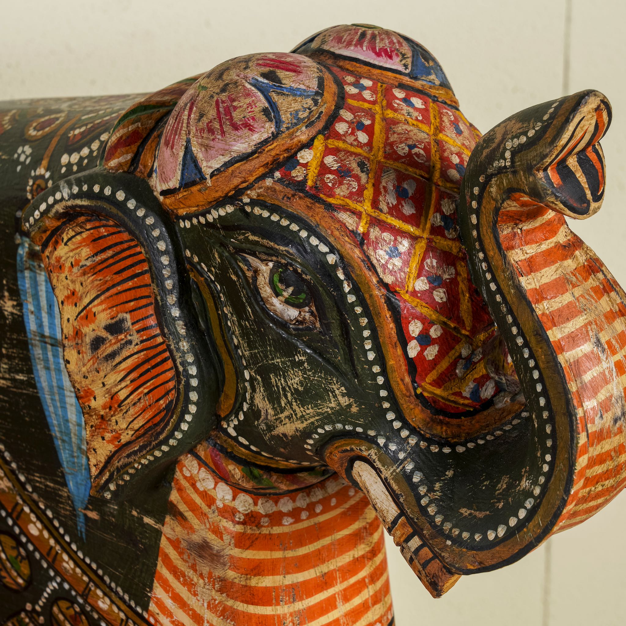 Close up image of a Elephant-shaped armchair crafted from reclaimed wood, featuring intricate hand-painted details in vibrant red, orange, green, and multi coloured floral patterns, with sculpted elephant head and legs for a whimsical, artistic touch.
