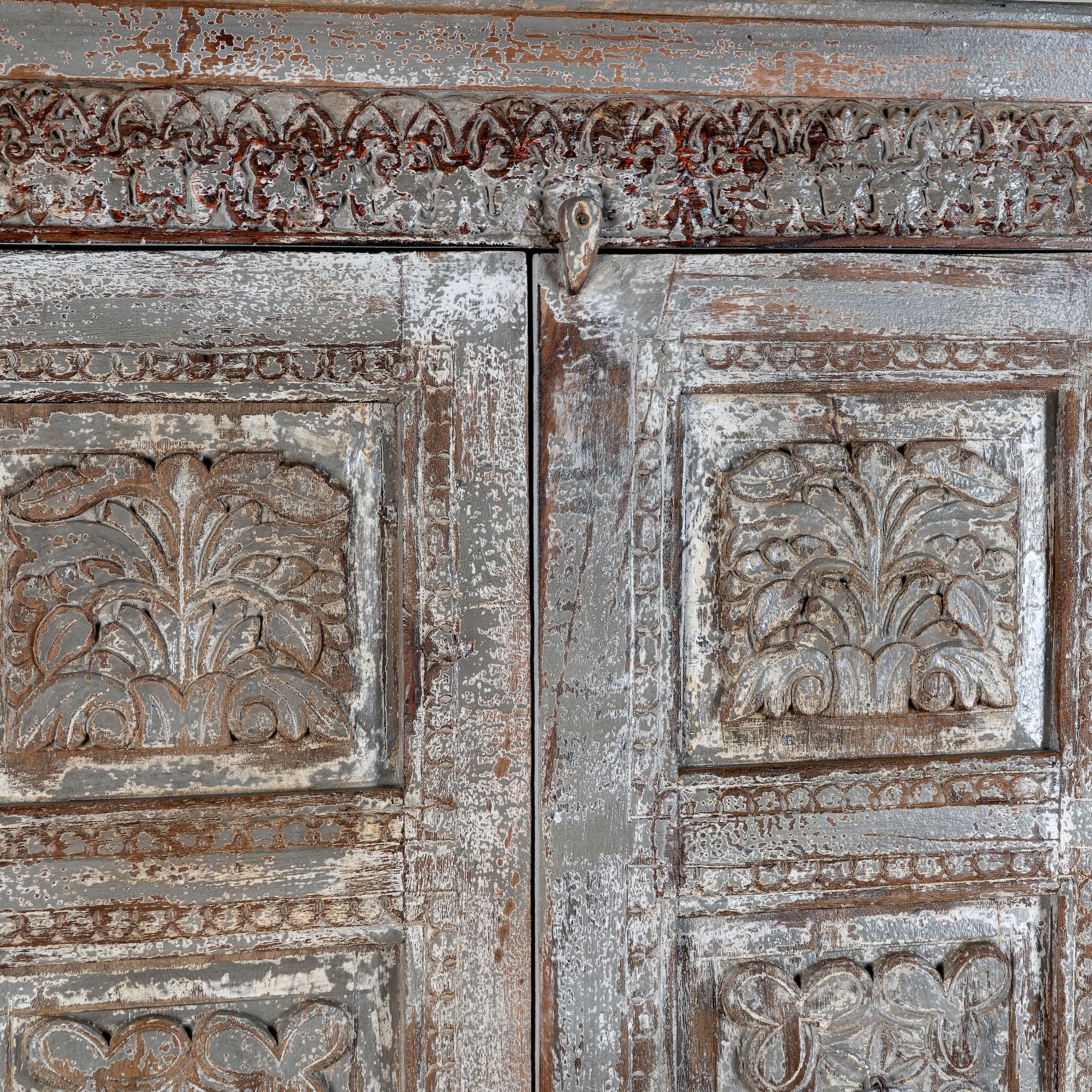 Close up image of a reclaimed teak wood cabinet Atharva with floral hand-carved doors in a vintage distressed finish. A sustainable furniture piece ideal for rustic and character-rich living room interiors.