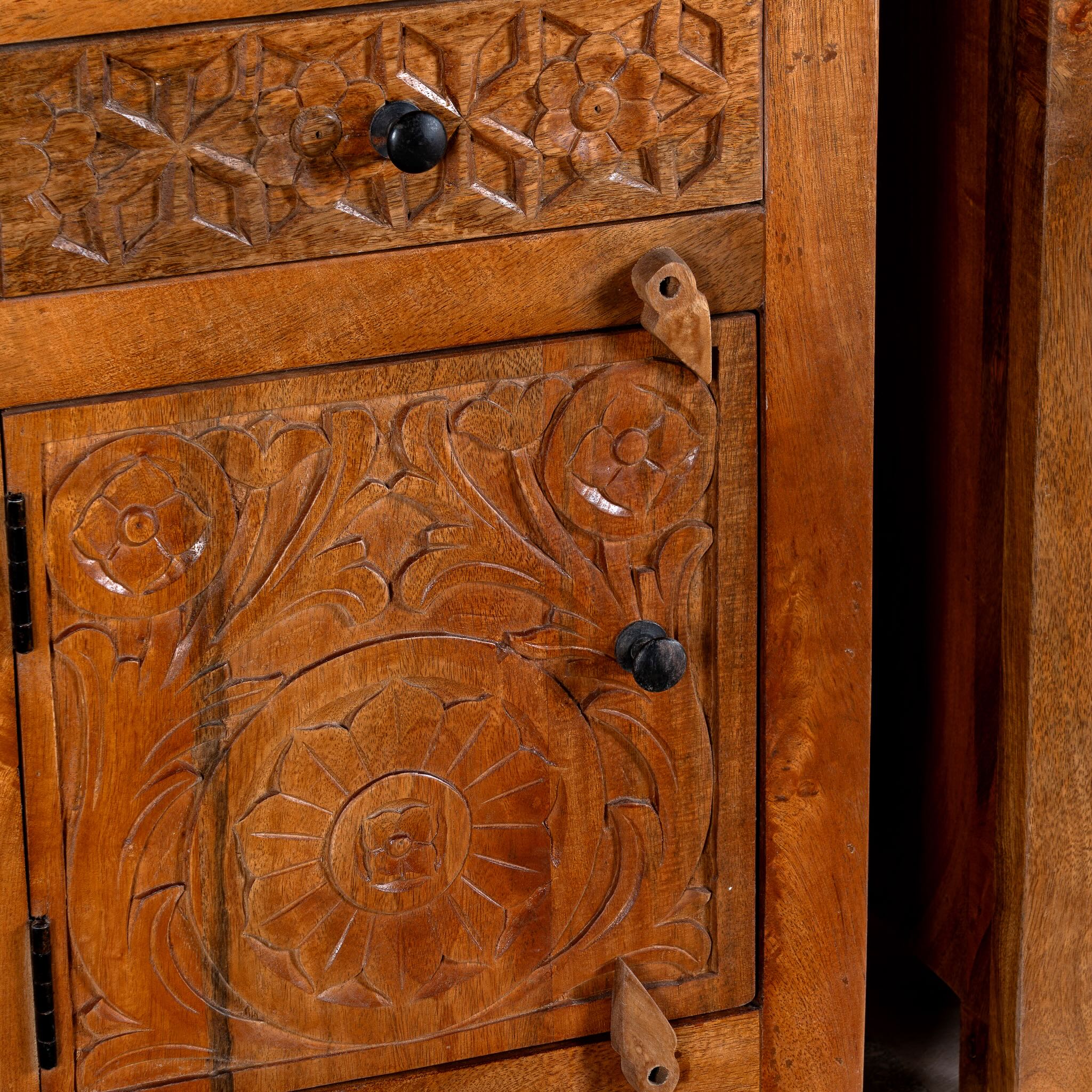 Close up image of a pair of handcrafted bedside tables Avi made from solid mango wood, featuring floral hand-carved motifs inspired by Ibiza style. Each table includes a drawer and a cabinet, with a natural wood finish that highlights artisanal detail and organic warmth.