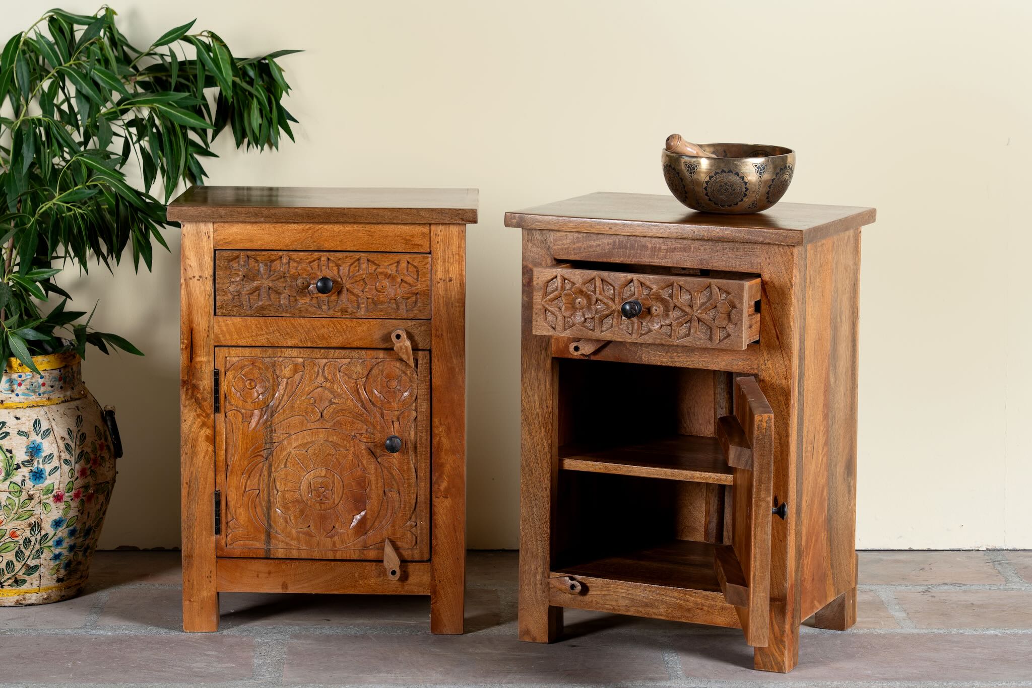 Side angle with open door image of a pair of handcrafted bedside tables Avi made from solid mango wood, featuring floral hand-carved motifs inspired by Ibiza style. Each table includes a drawer and a cabinet, with a natural wood finish that highlights artisanal detail and organic warmth.
