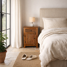 Lifestyle image of a handcrafted bedside table Avi made from solid mango wood, featuring floral hand-carved motifs inspired by Ibiza style. Each table includes a drawer and a cabinet, with a natural wood finish that highlights artisanal detail and organic warmth.