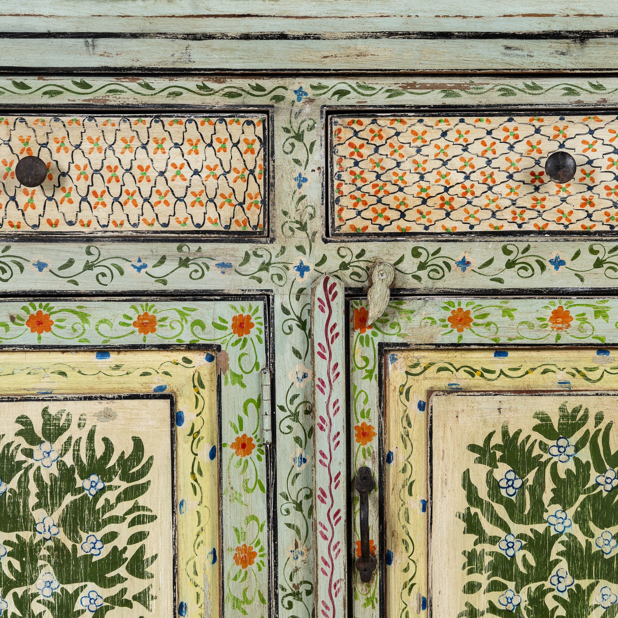 Close up image of a hand-painted sideboard made from reclaimed wood, featuring three drawers and three cabinet doors adorned with intricate floral borders and tree motifs in earthy green and warm tones, finished in a soft distressed patina for a vintage artisanal look.
