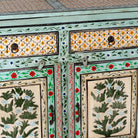 Close up image of a hand-painted sideboard made from reclaimed wood, featuring three drawers and three cabinet doors adorned with intricate floral borders and tree motifs in earthy green and warm tones, finished in a soft distressed patina for a vintage artisanal look.
